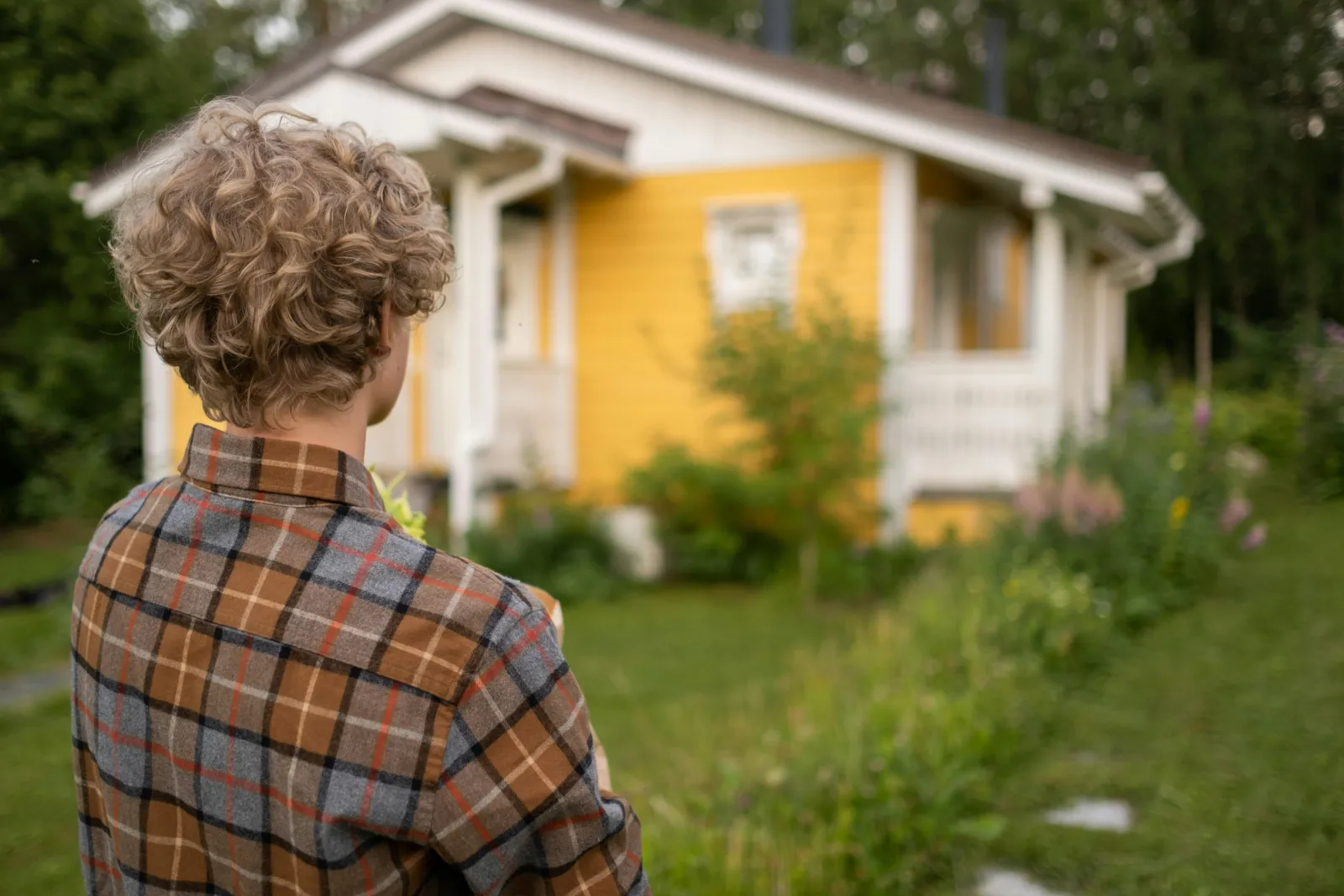 Ungdom på vei mot et gult hus med frodig hage en sommerdag