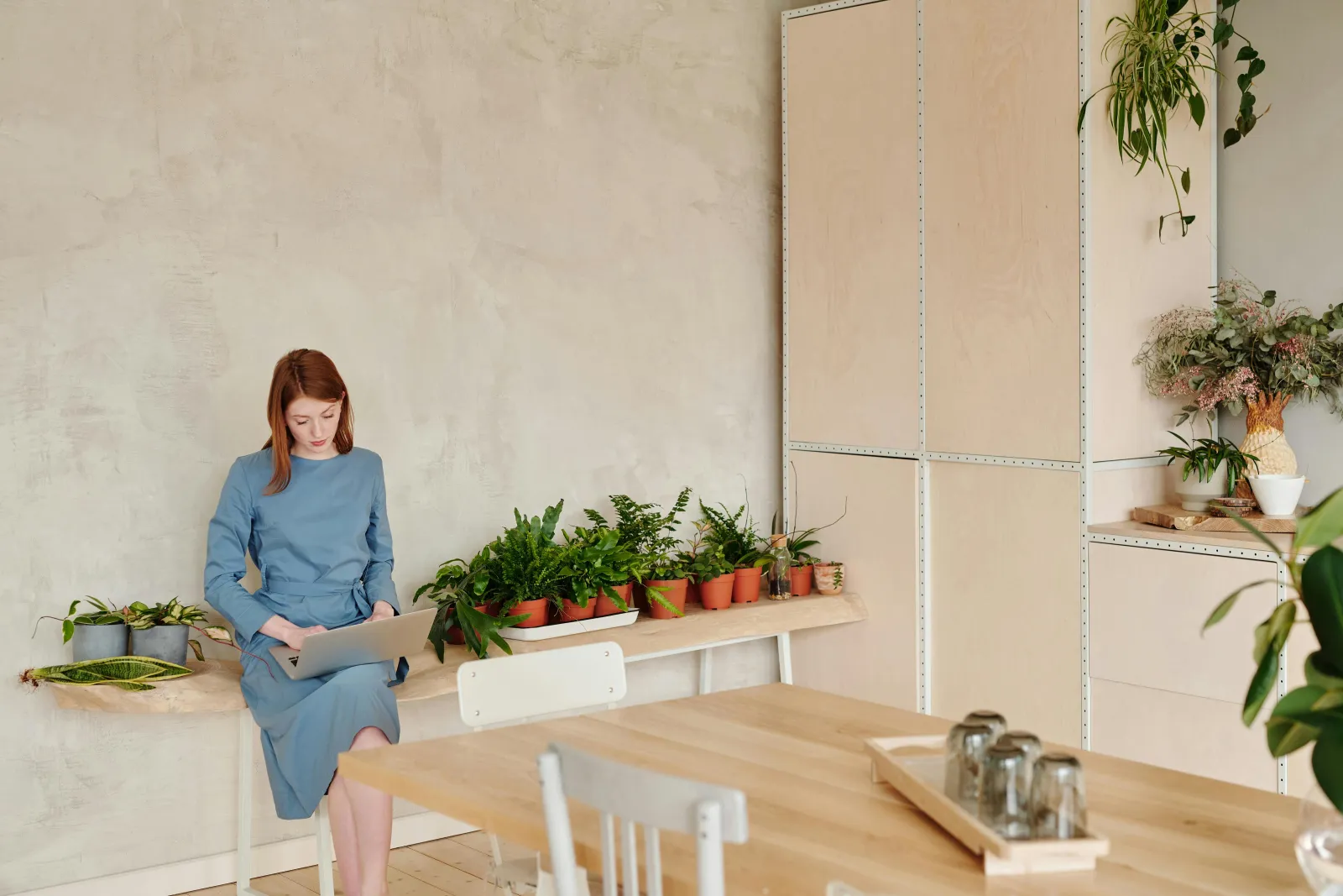 Ung kvinne ved en trepult med laptop og planter i et lyst rom